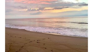 Ein Strand mit Fußspuren im Sand und einem Sonnenuntergang im Hintergrund.