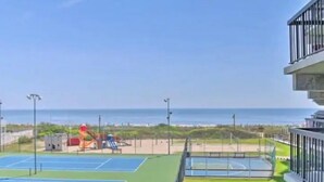 Ein Tennisplatz mit einem Spielplatz im Hintergrund, einem klaren Himmel und Blick auf den Ozean.