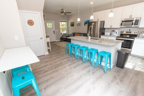 A modern kitchen with a central island, bar stools, stainless steel appliances, and a ceiling fan.