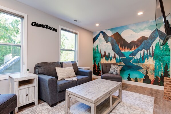 A cozy living room with a gray sofa, a white coffee table, and a mural of a mountain landscape on the wall.