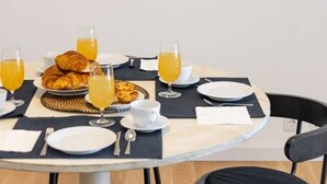 A dining table set with croissants, glasses of orange juice, and a plate of food, surrounded by chairs and framed artwork on the wall. - Ajuda · Belvedere TM Flat With a Magnificent View (Lisboa)