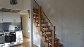 Eine moderne Küche mit Einbauofen und Kaffeemaschine, einer Holztreppe und einem hellen Essbereich.