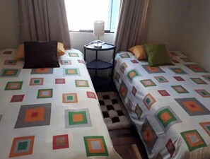 A hotel room with two beds, each with a patterned bedspread and pillows. There is a small table with a lamp between the beds. - Modern for 6 people, queen beds, wi fi, neflix (Cusco)