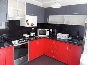 A kitchen with red cabinets, a black countertop, a stove, a microwave, and a sink. - Modern for 6 people, queen beds, wi fi, neflix (Cusco)