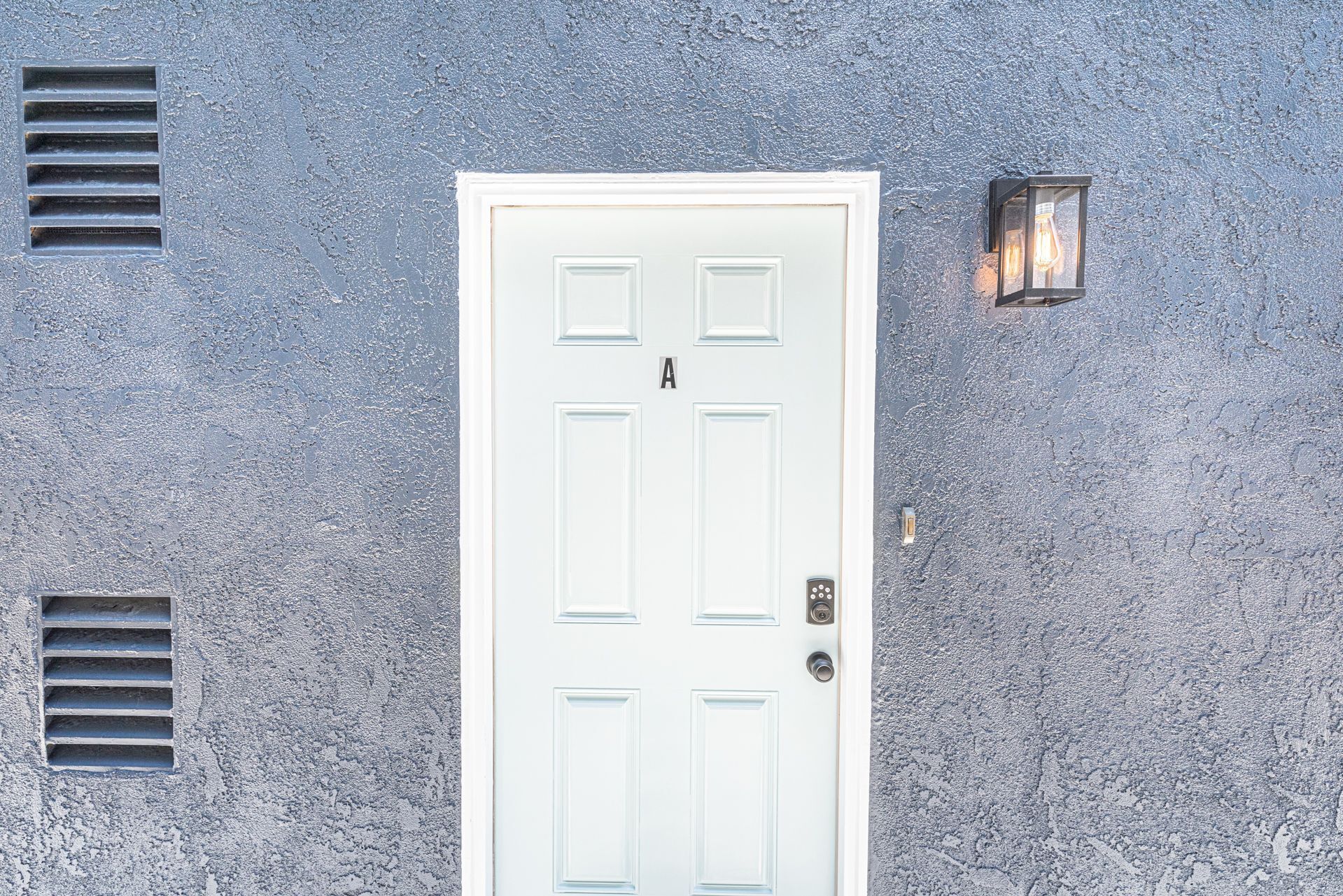 A white door with a keypad lock, flanked by two vents on a textured blue wall.