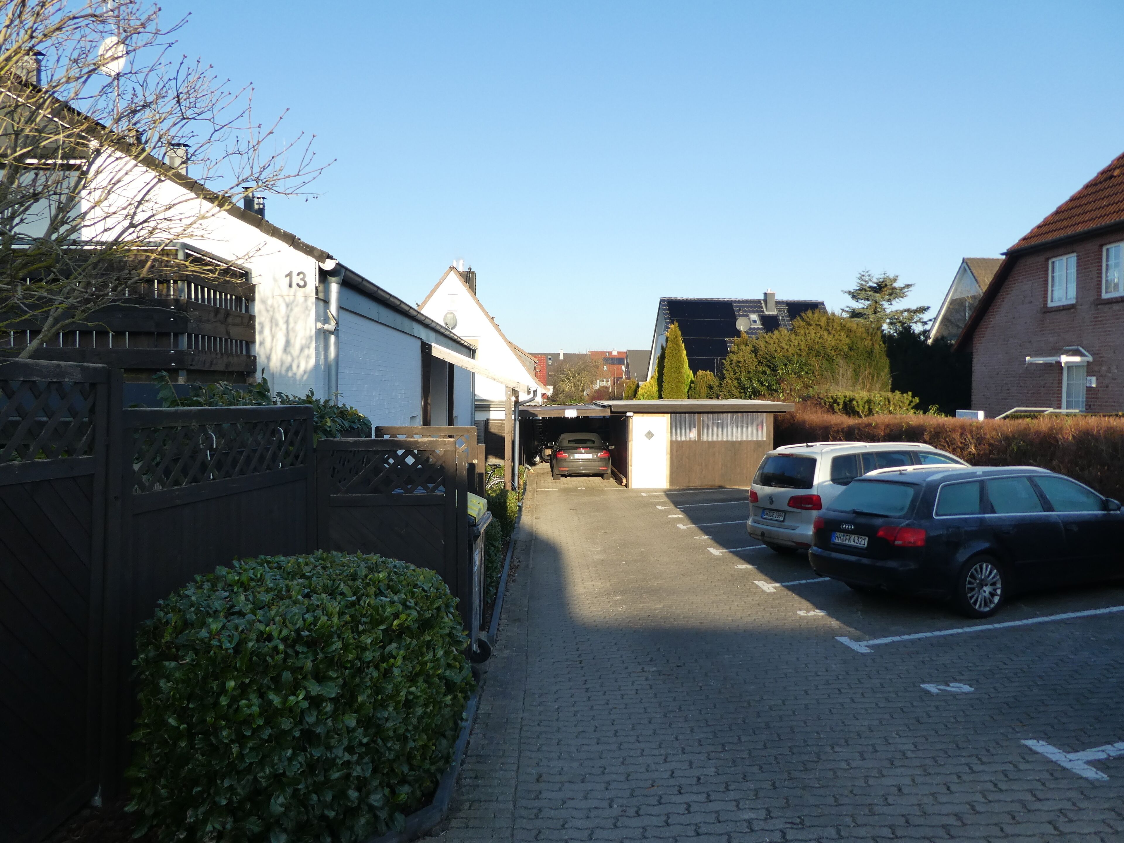 A residential street with parked cars, a small shed, and a house with a number 13 on its facade.