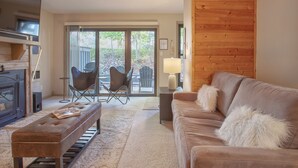Sala de estar con sofá, reposapiés y chimenea. Hay una puerta corrediza de vidrio que da a un espacio exterior con sillas.