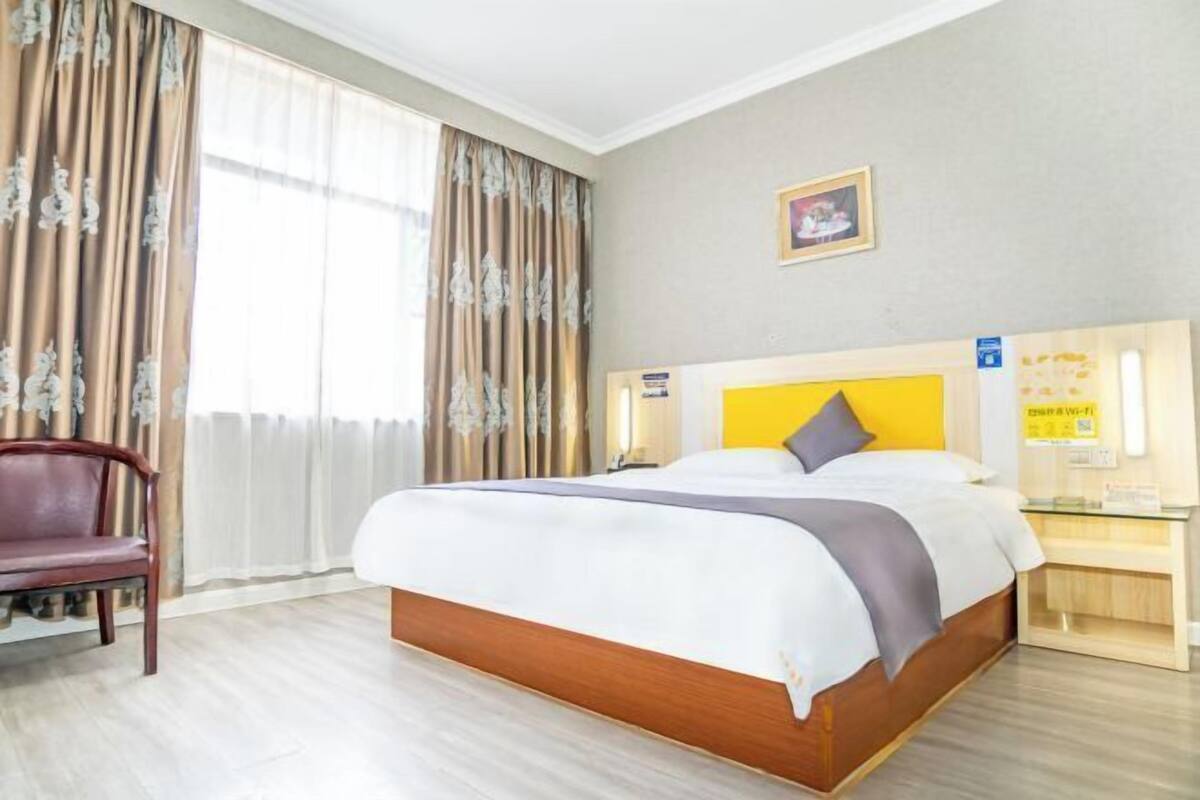 A hotel room with a bed, a chair, a bedside table, and a window with curtains.