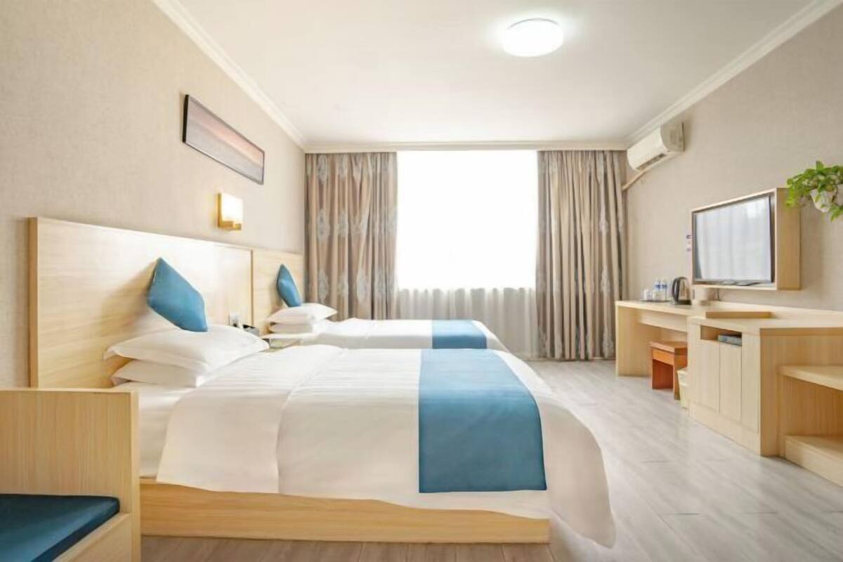 A hotel room with two beds, a desk, a TV, and a window with curtains.