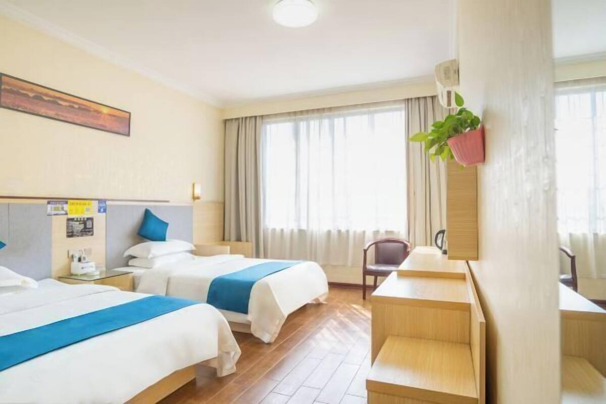 A hotel room with two beds, a desk, a chair, and a large window with curtains.