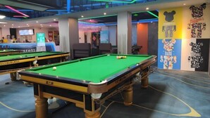 A pool hall with multiple pool tables, a seating area, and a wall with various posters. - Hezhou Xintai Hotel (Hezhou)