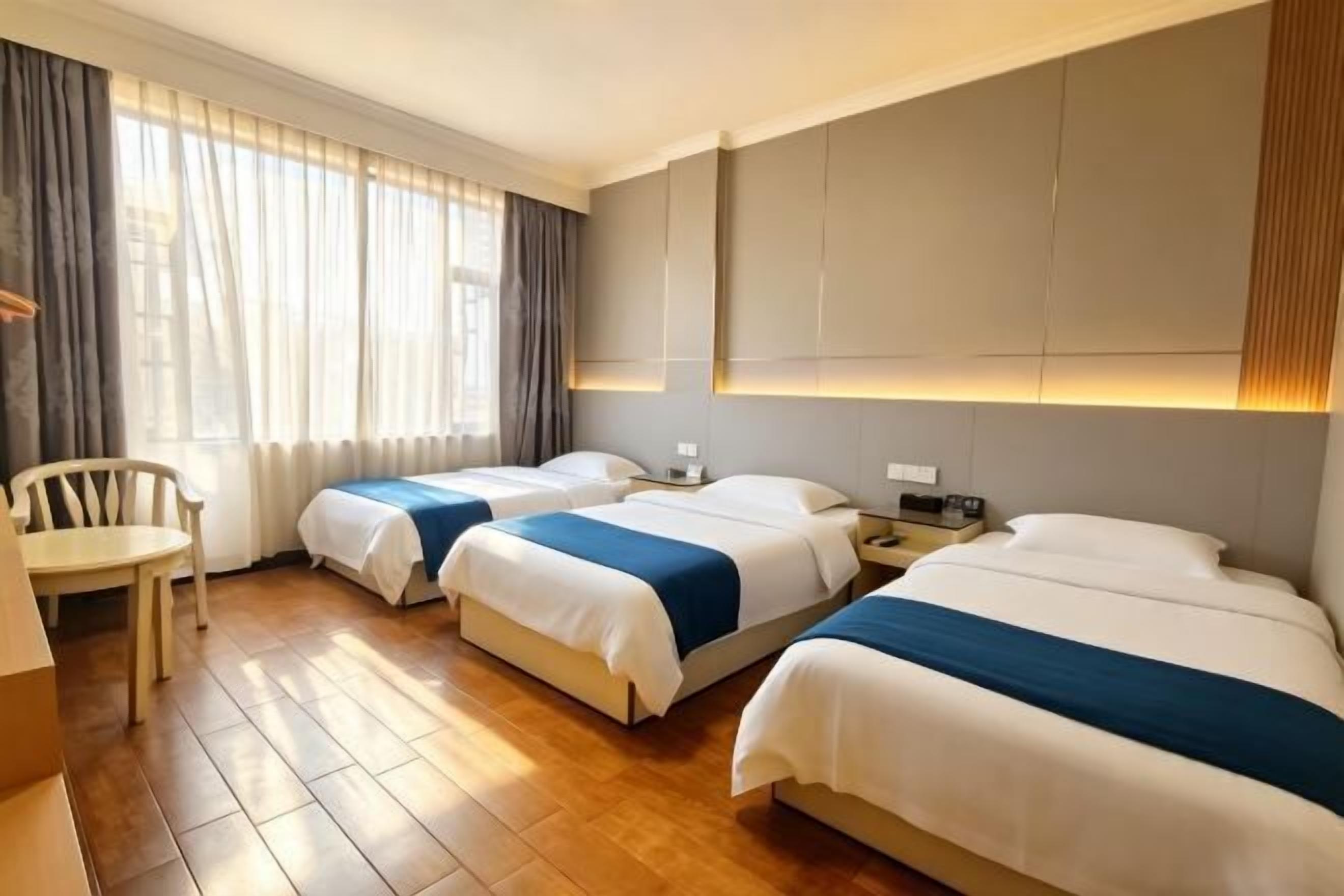 A hotel room with three beds, a wooden floor, a desk, and a chair.