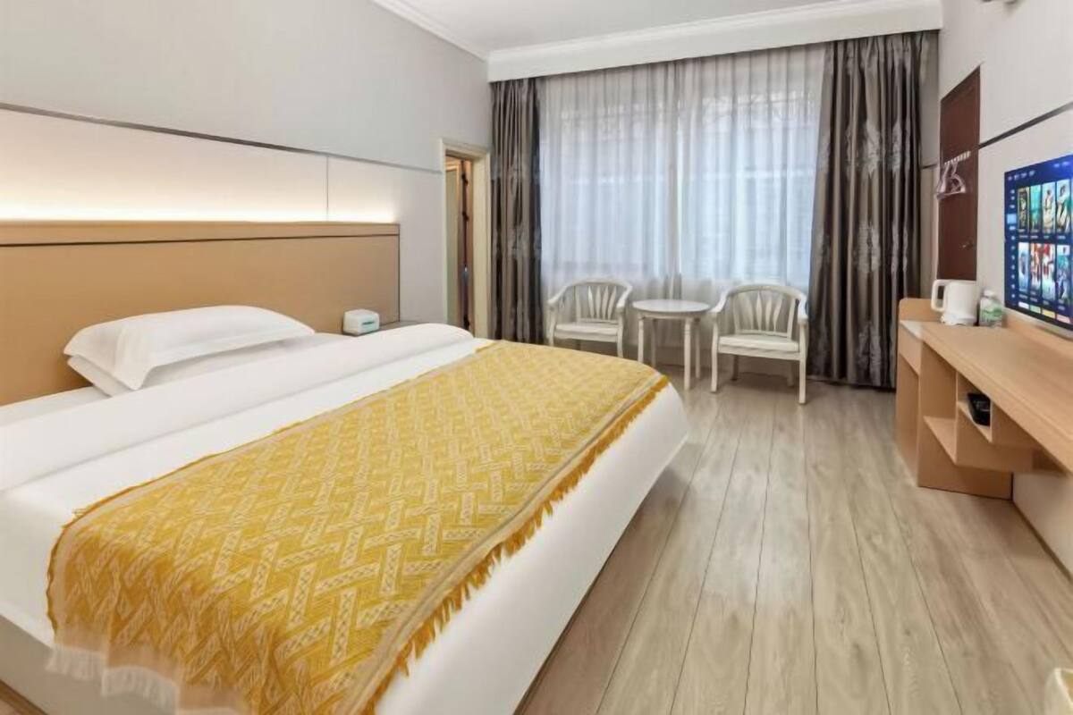 A hotel room with a large bed, a bedside table, a TV, a desk, and a chair.