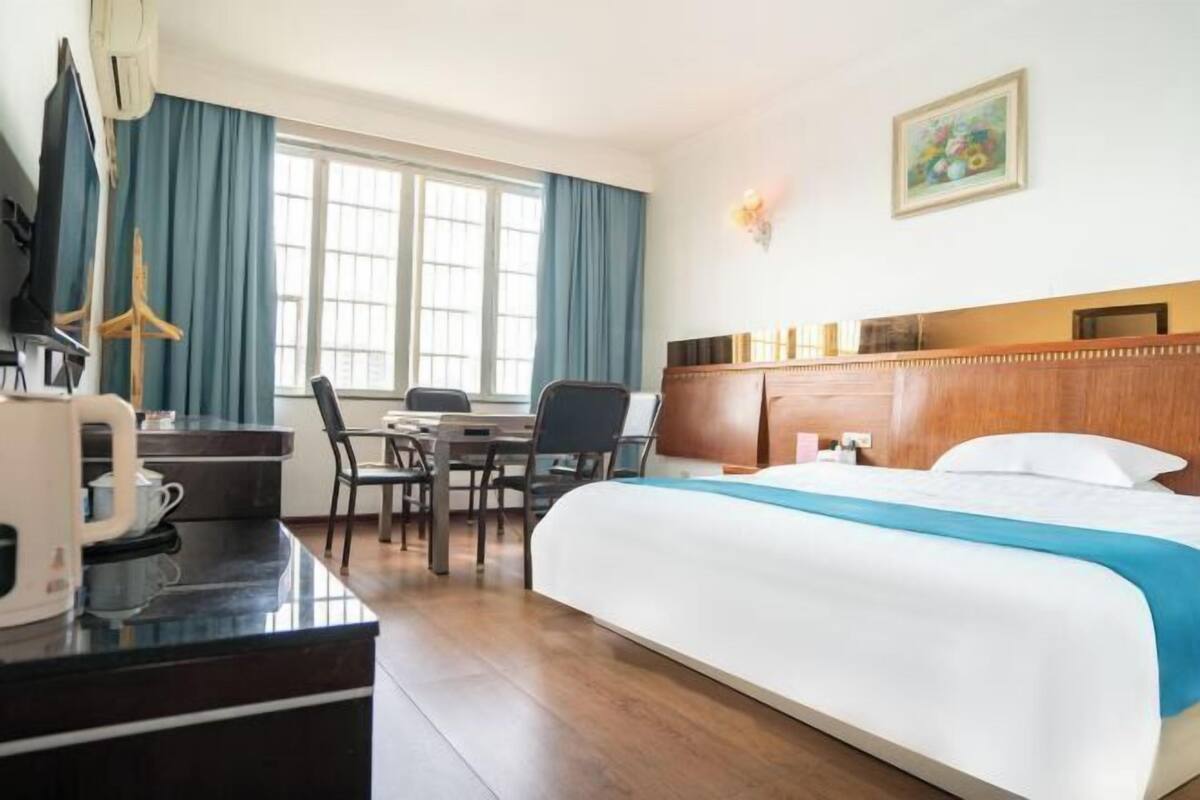 A hotel room with a bed, a desk with a chair, a television, and a window with curtains.