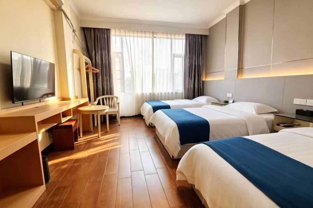 A hotel room with a TV, a desk, a chair, two beds, and a window with curtains.
