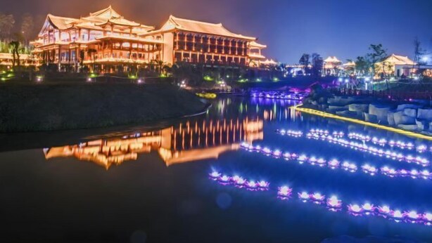 A traditional building with a reflection in a calm body of water, illuminated by colorful lights. - Hezhou Xintai Hotel (Hezhou)