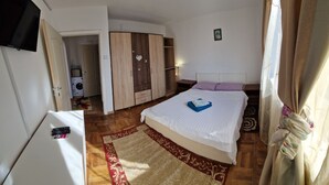 Ein Schlafzimmer mit Bett, Schrank, Fernseher und einer Waschmaschine im Hintergrund.