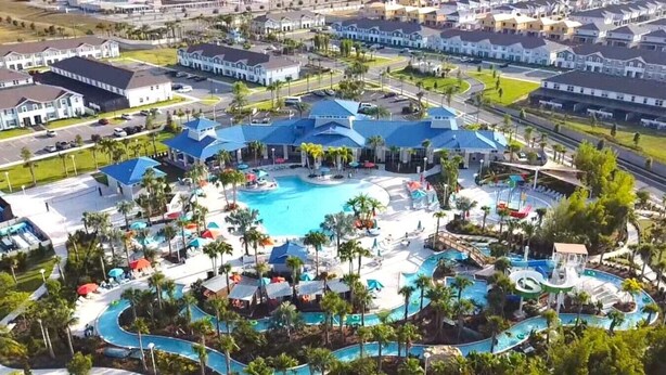 Luchtbeeld van een resort met meerdere zwembaden, palmbomen en een groot gebouw met een blauw dak.