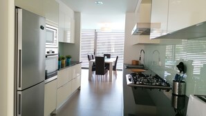 A modern kitchen with stainless steel appliances, a dining area with a table and chairs, and a view through large windows. - Seaview and private pool - house for 6 (Lourinhã)