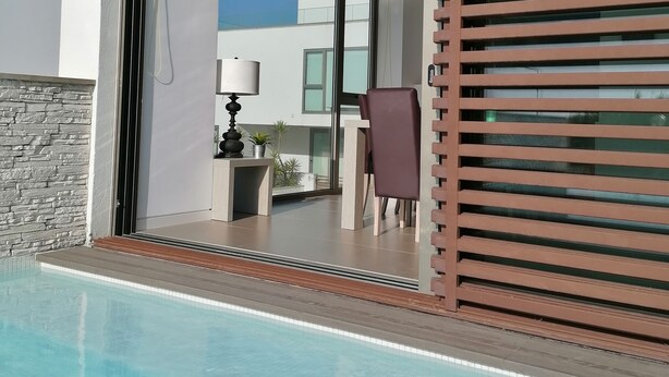 A modern poolside area with a clear view of the pool, a seating area with a chair and table, and a large sliding glass door leading to an outdoor space. - Seaview and private pool - house for 6 (Lourinhã)