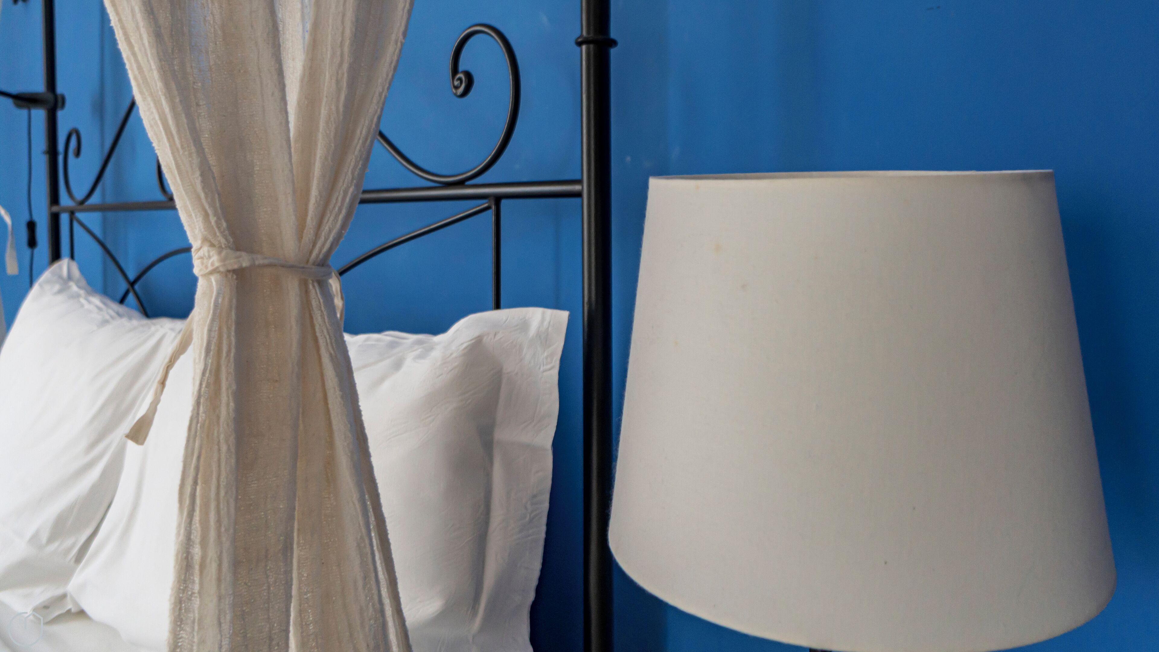 A bed with white bedding and a black metal frame against a blue wall.