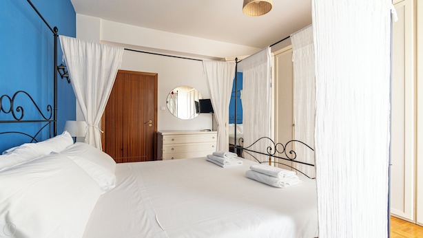 Une chambre bien éclairée, avec un grand lit, une armoire en bois, une table de chevet et un miroir.