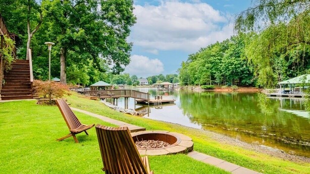 Un patio junto al lago con sillas de madera, una chimenea y un muelle que se adentra en el agua.