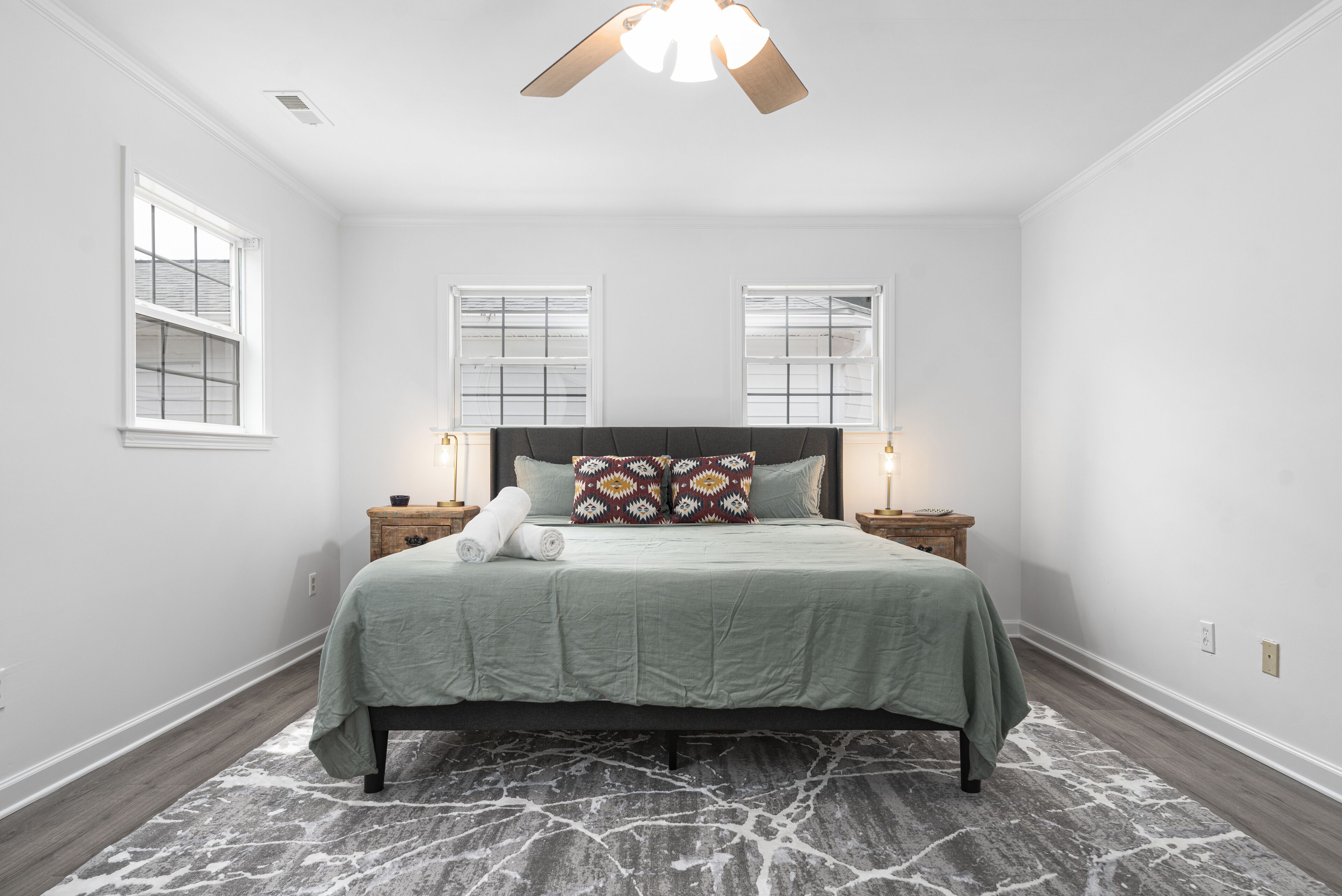 A bedroom with a bed, two bedside tables, a ceiling fan, and two windows.