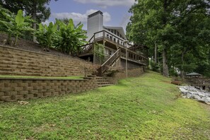 A house with a stone retaining wall, a wooden staircase, and a large tree.