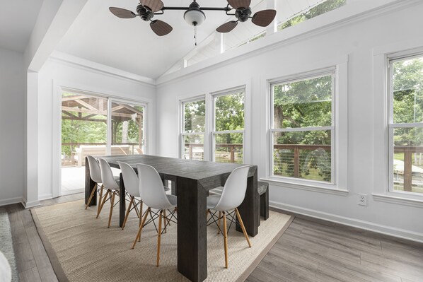 A dining area with a dark wooden table, white chairs, and a ceiling fan.