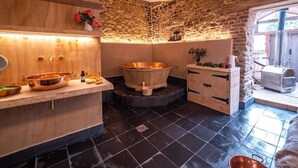 A spa room with a wooden vanity, a copper bathtub, and a stone wall.