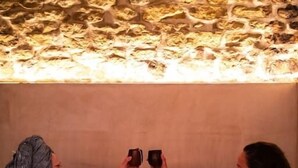 Two people in a wooden bathtub with a stone wall behind them.
