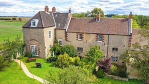A large stone house with a tiled roof, surrounded by a well-maintained garden and a clear sky.