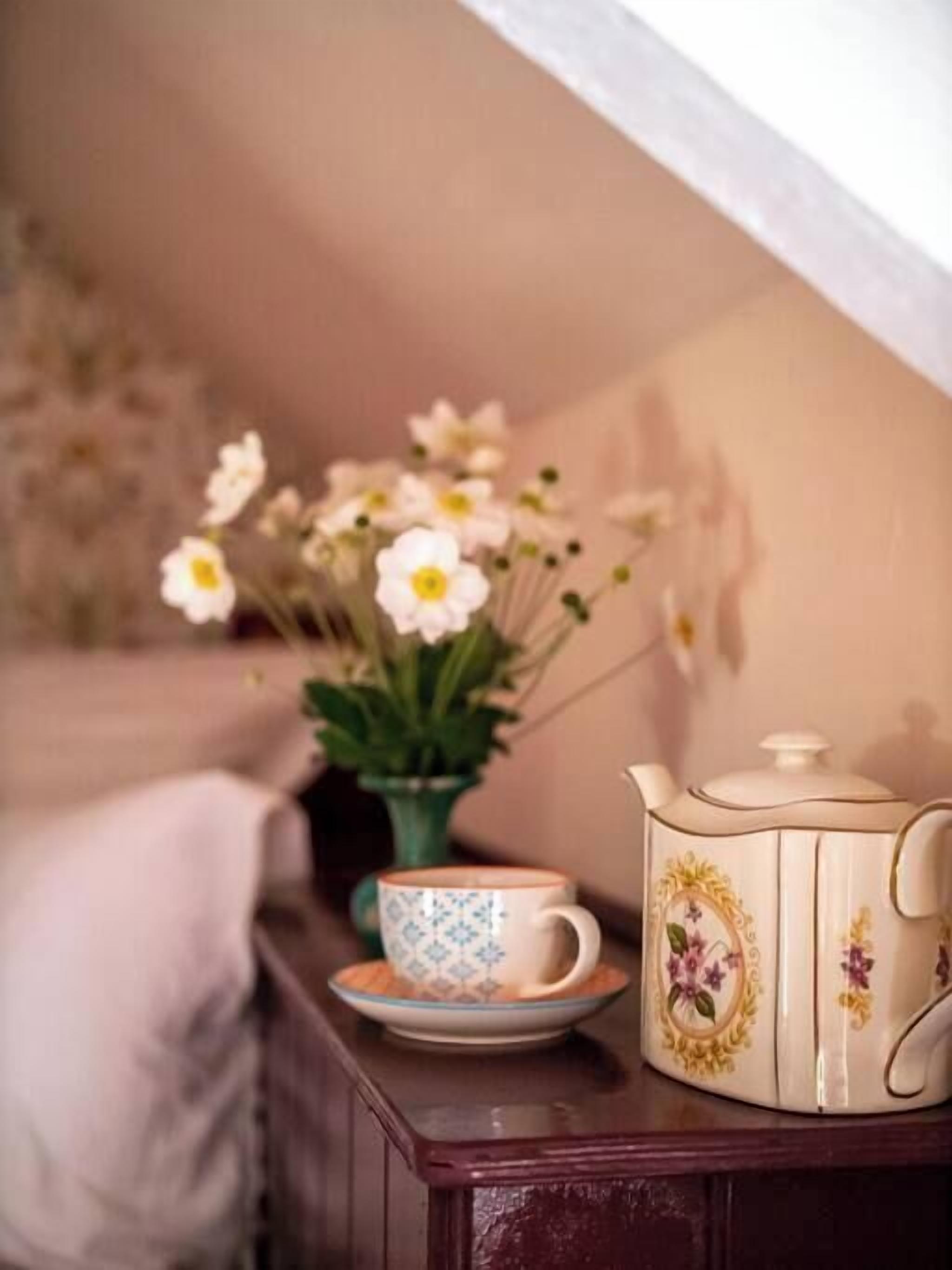 Une pièce chaleureuse avec une table en bois, une théière, une tasse et un vase rempli de fleurs.
