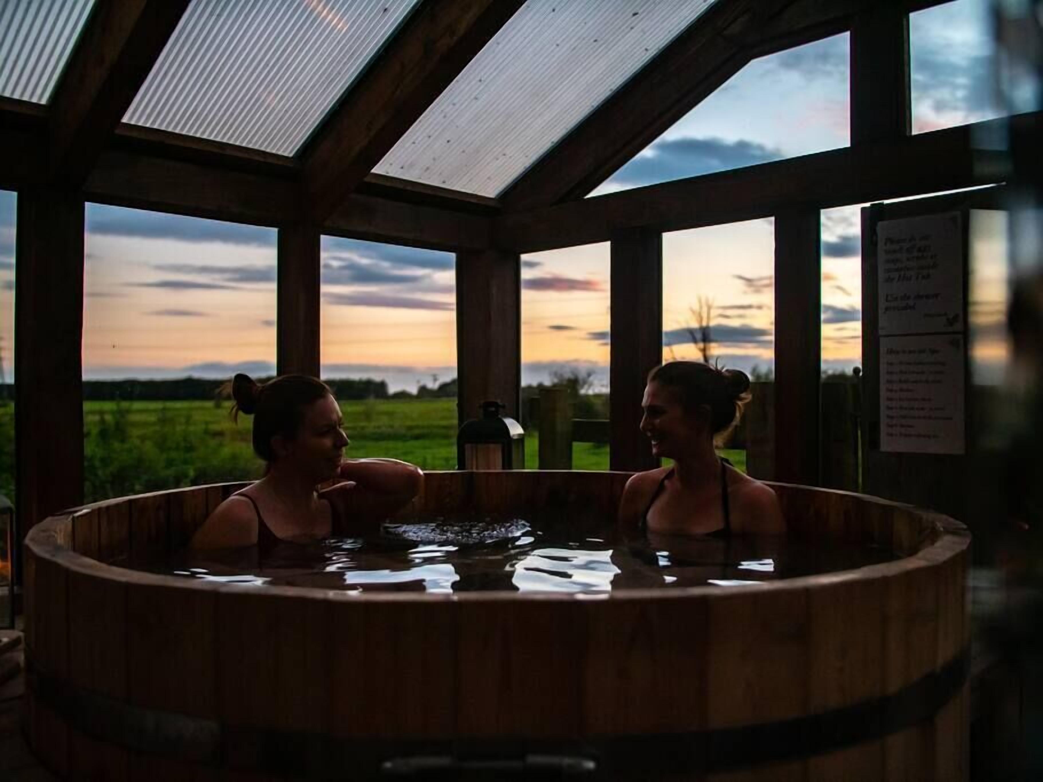 A wooden hot tub with a view of a sunset over a green field.