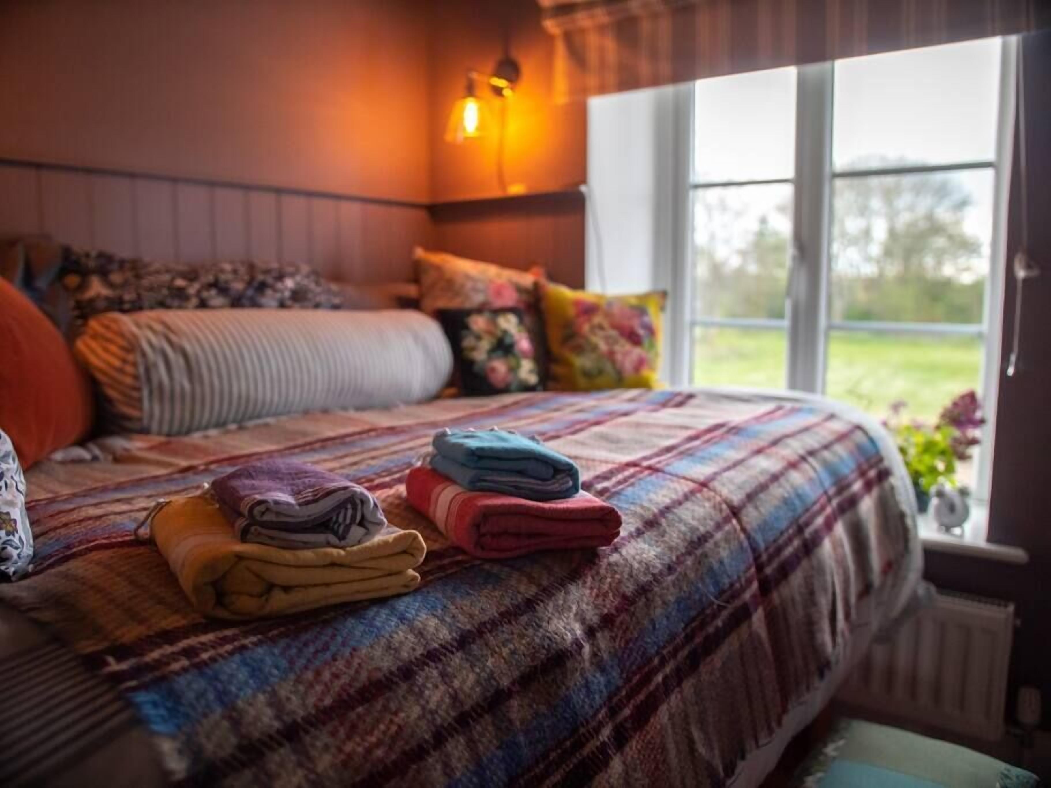 A neatly made bed with a plaid bedspread and folded blankets in various colors.
