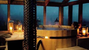 Un bain à remous dans un chalet en bois doté de grandes fenêtres et de lanternes.