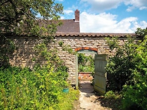 Set amidst lush gardens, this charming stone building features a traditional tiled roof and a stone archway entrance.