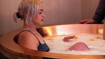 Una donna in una vasca da bagno di legno con una persona accanto.
