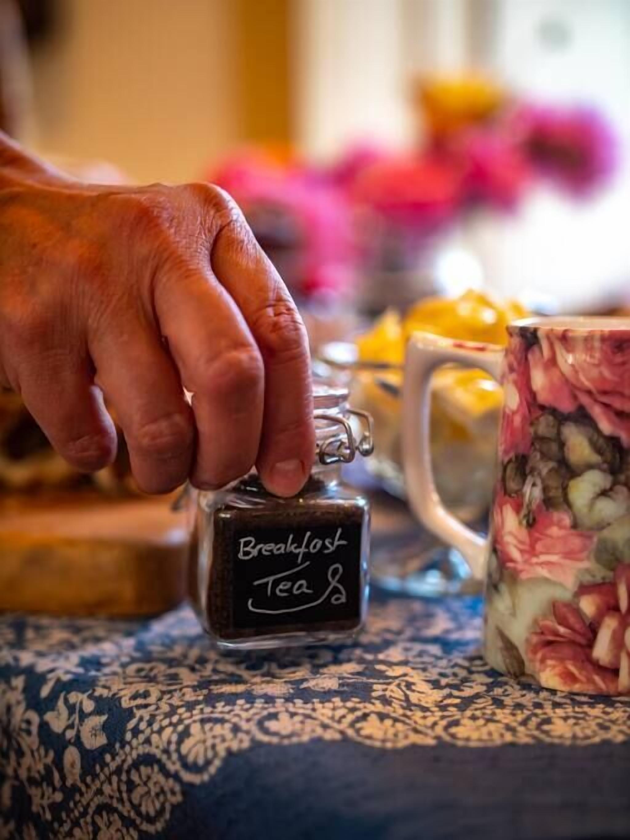A hand holding a small bottle labeled "Breakfast Tea" on a patterned tablecloth.