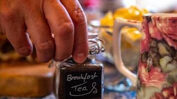 A hand holding a small bottle labeled "Breakfast Tea" on a patterned tablecloth.