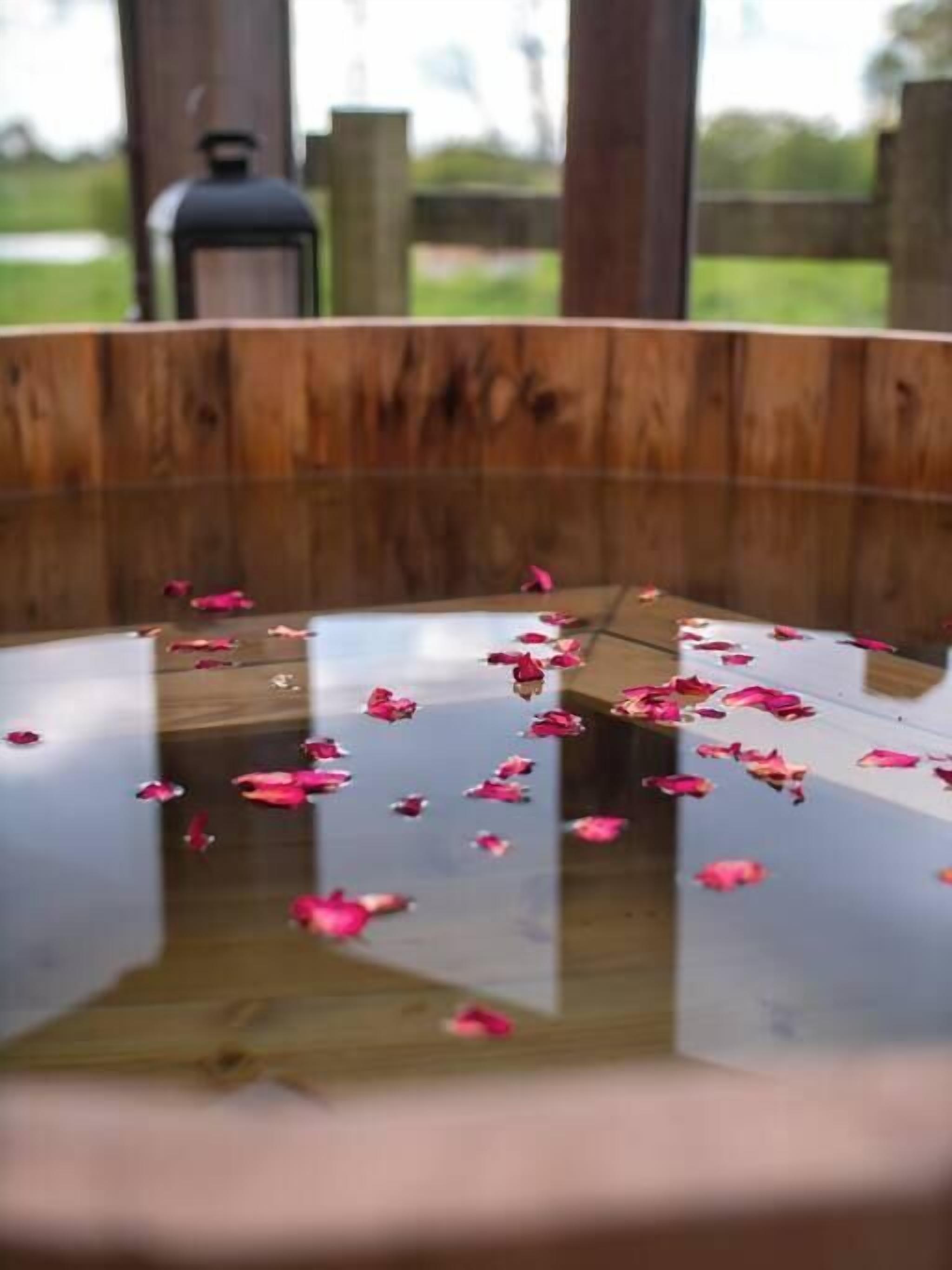 Une structure circulaire en bois, dotée d’une surface réfléchissante et parsemée de pétales roses.