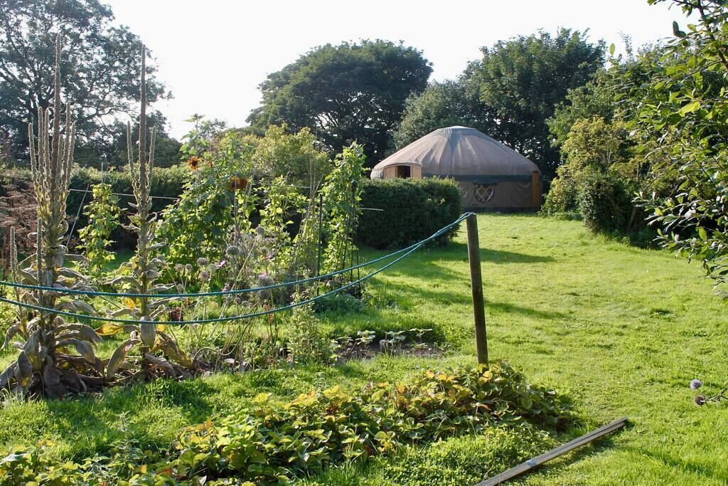 Eine Jurte in einem Garten mit einem Seilzaun, umgeben von Grünflächen und Bäumen.