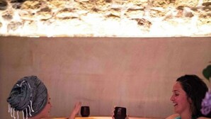 Two people in a wooden hot tub with a stone wall behind them. - Library Suite: Sleeps 4 (Scunthorpe)