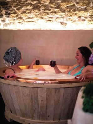 Two people in a wooden hot tub with a stone wall behind them. - Library Suite: Sleeps 4 (Scunthorpe)