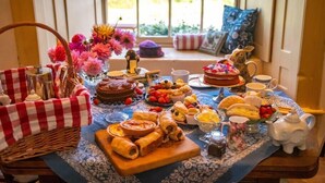 A table set with various food items, a cake, and a teapot, with a window view in the background. - Library Suite: Sleeps 4 (Scunthorpe)