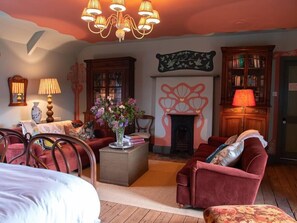 Une pièce chaleureuse avec une cheminée, un canapé, une table ornée d’un vase de fleurs et une bibliothèque.