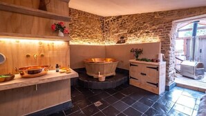 A spa room with a wooden vanity, a stone wall, a wooden bathtub, and a stone floor. - Library Suite: Sleeps 4 (Scunthorpe)