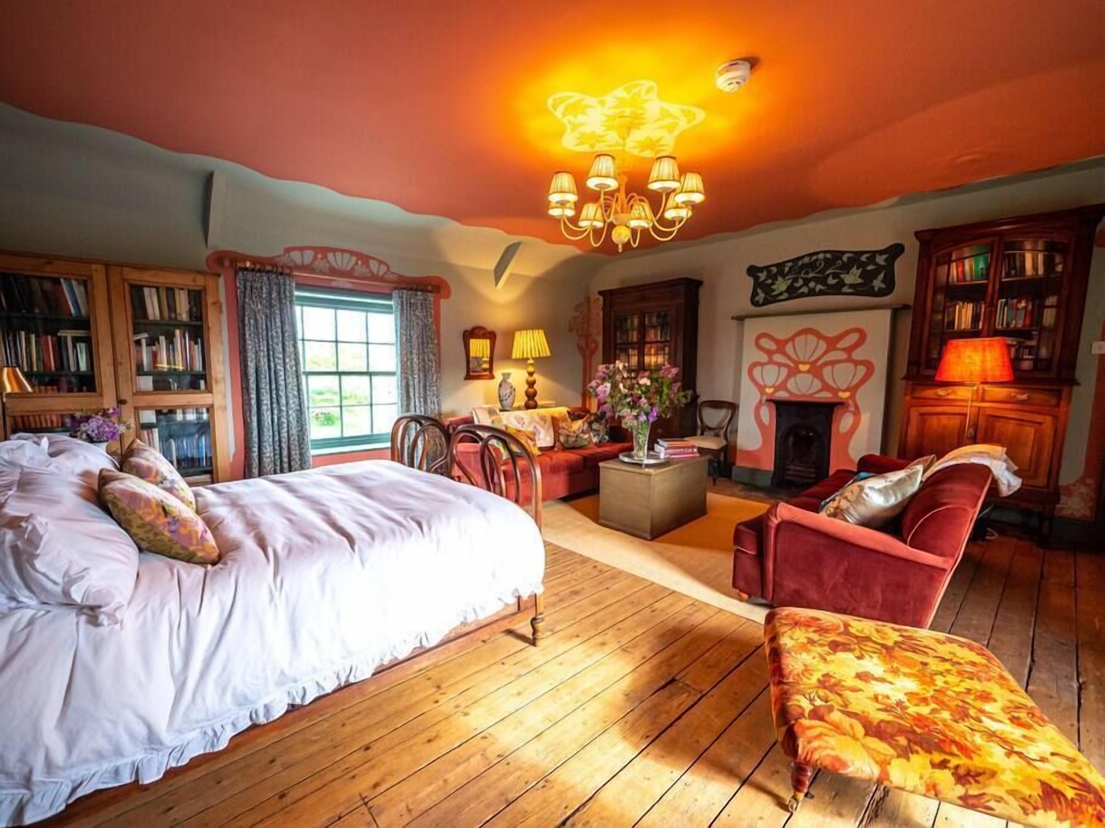 Une chambre spacieuse avec un grand lit, un coin salon comprenant un canapé et des fauteuils, une cheminée et une bibliothèque.
