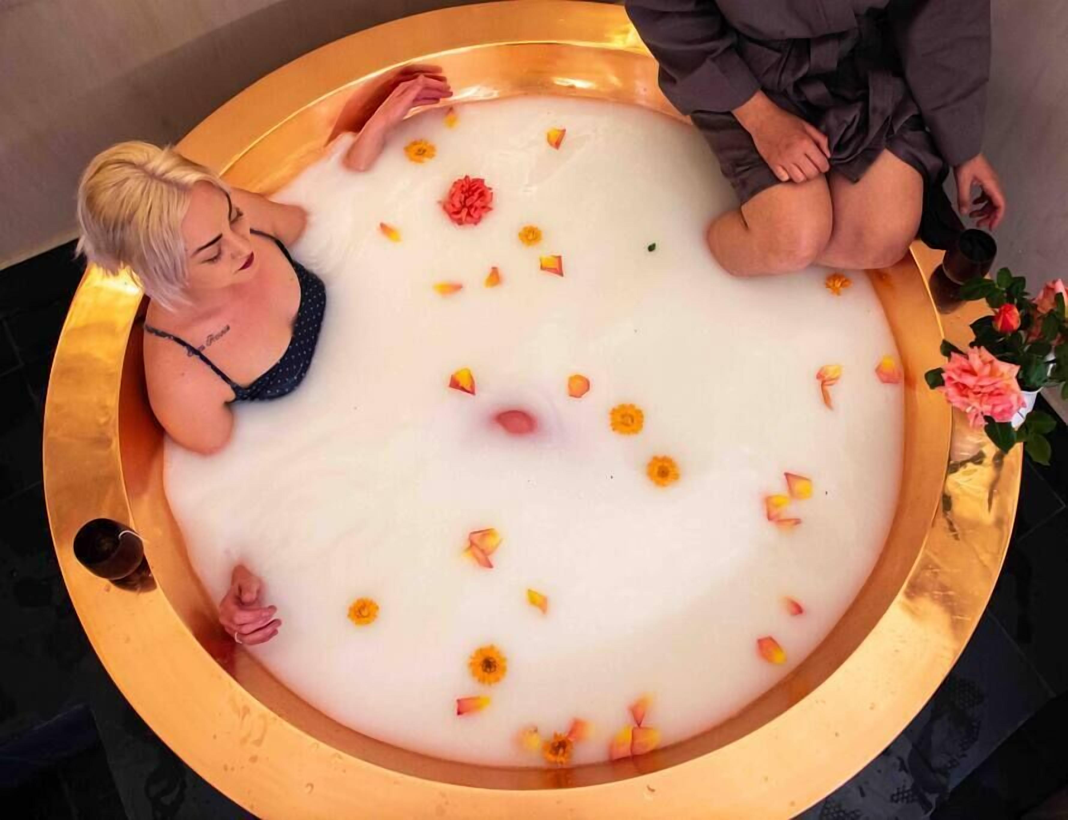 A bathtub filled with white liquid and flower petals, surrounded by a golden frame.